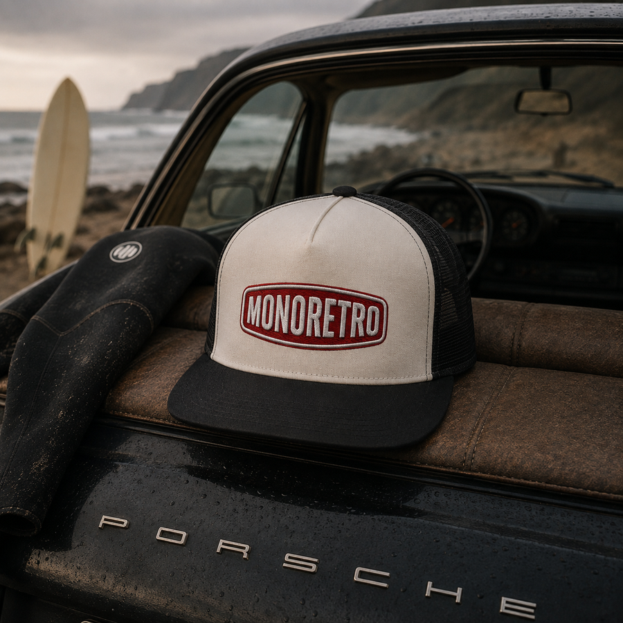 MONORETRO trucker cap in cream and navy resting on a wetsuit, on the rear of a Porsche beside a surfboard.