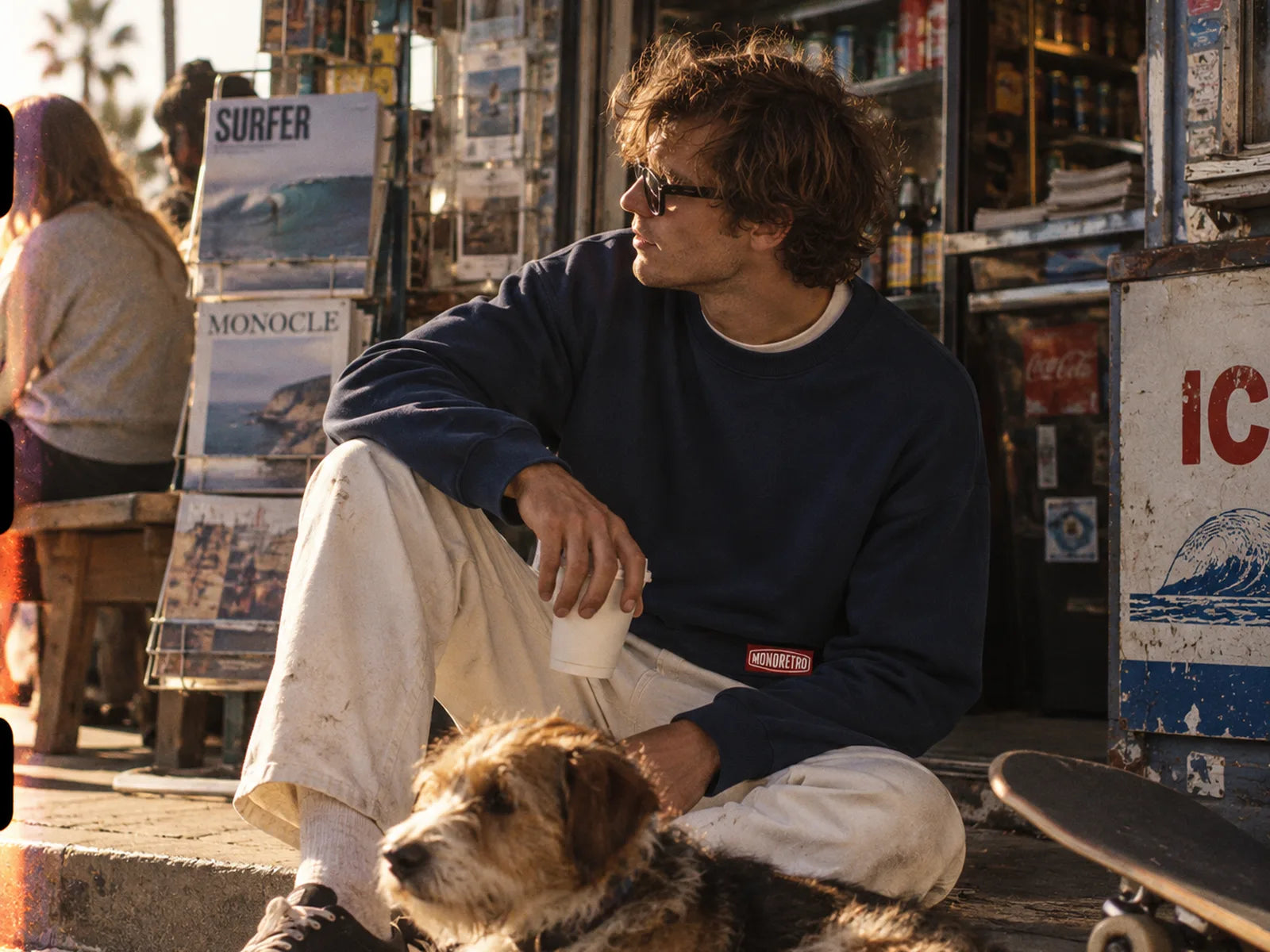 A man sitting outside a kiosk with a coffee and a dog
