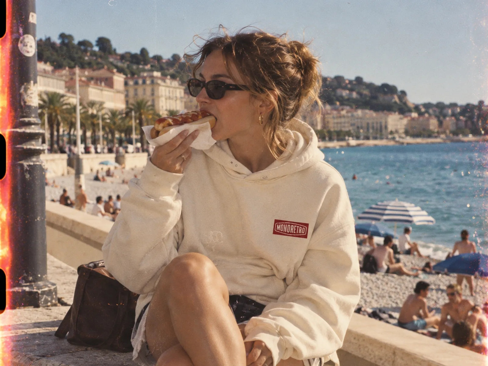 A woman eating a hot dog on the sea wall above a beach